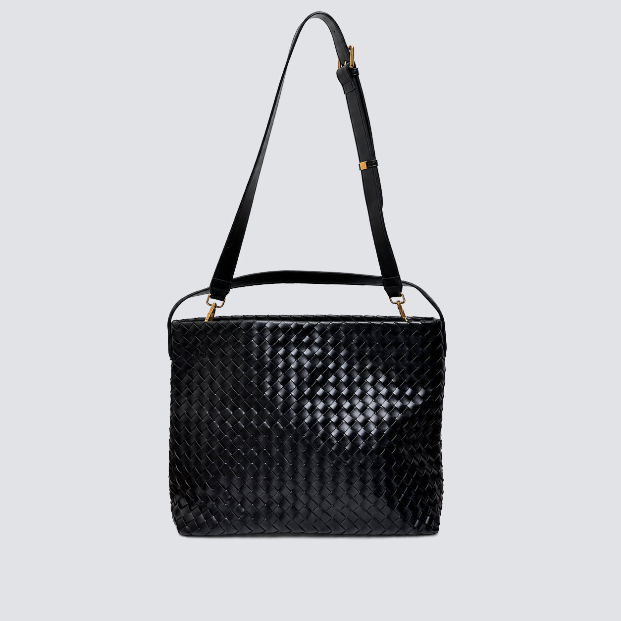 Black woven tote bag displayed with its long adjustable crossbody strap attached