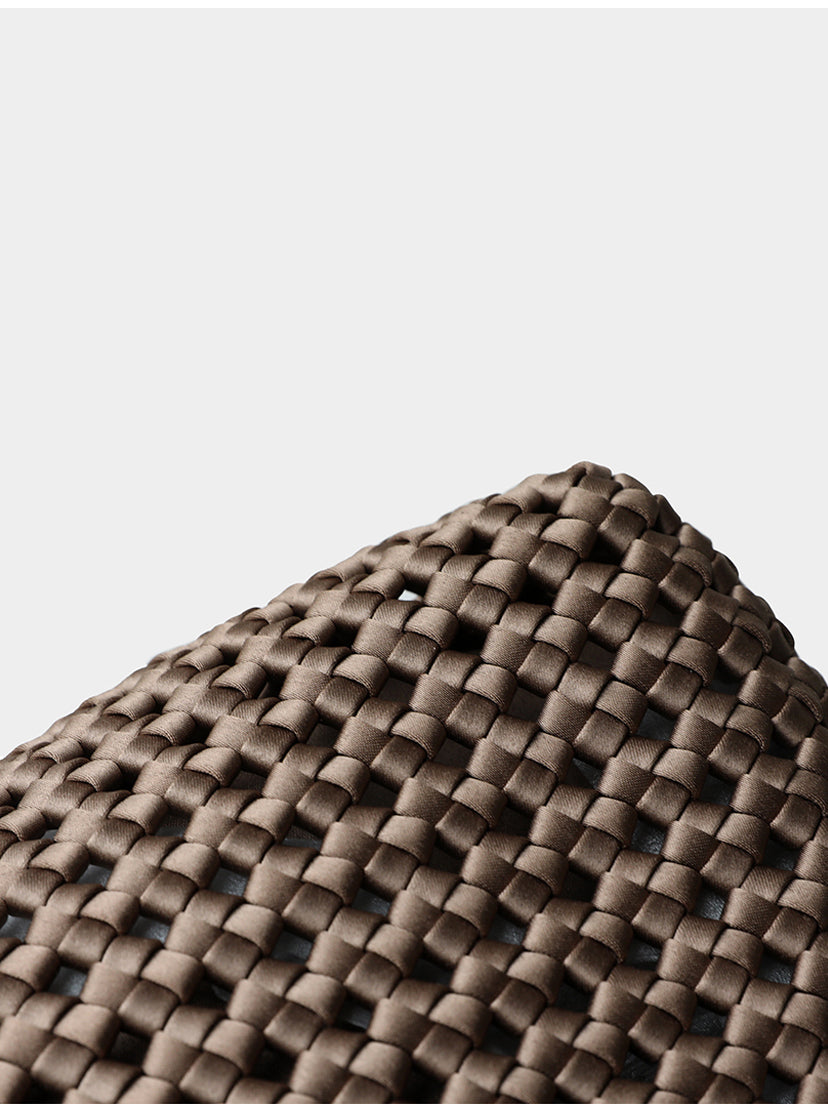 Macro close-up of the meticulous hollow lattice woven texture on the brown genuine leather tote bag.
