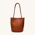 Front view of a cognac brown woven vegan leather bucket bag with slim shoulder straps