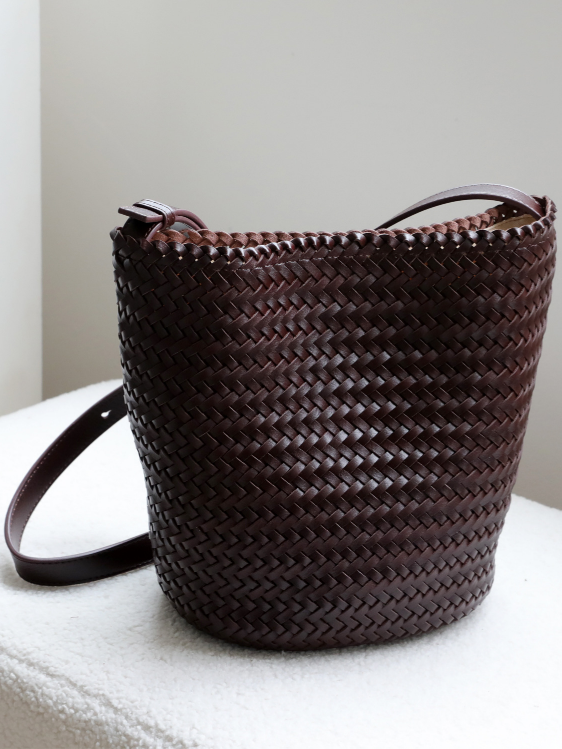 Elegant dark chocolate brown handwoven vegan leather bucket bag featuring a sleek adjustable strap and minimalist structured design.