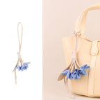 Blue vegan leather flower bag charm with beige stem attached to a cream handbag handle