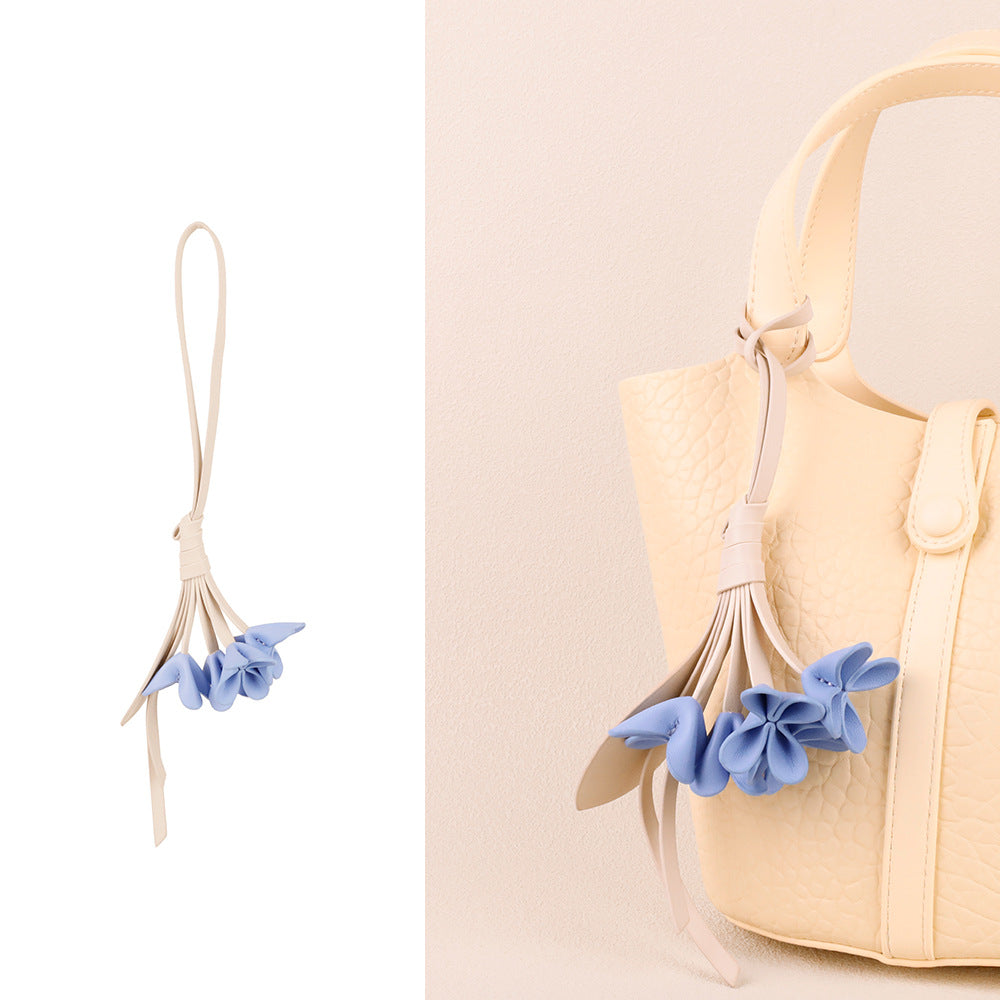 Blue vegan leather flower bag charm with beige stem attached to a cream handbag handle