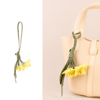 Yellow vegan leather flower bag charm with olive green stem attached to a cream handbag handle