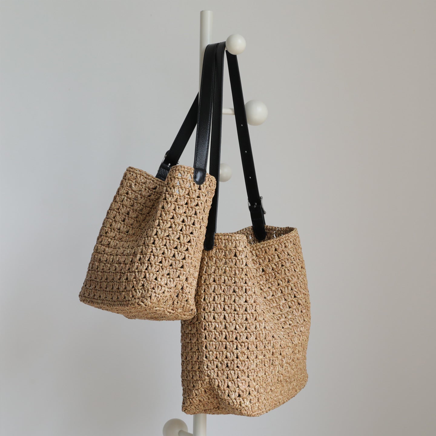 Woven raffia bucket bags hanging by their black genuine leather straps