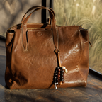 Minimalist leather and natural seed bag charm attached to a brown tote bag.