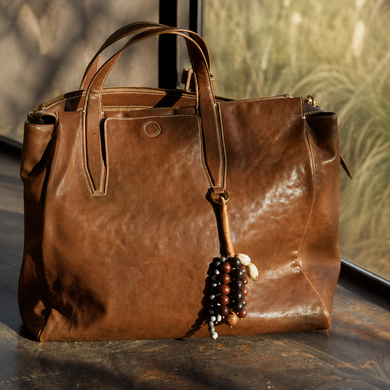 Minimalist leather and natural seed bag charm attached to a brown tote bag.