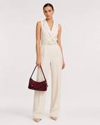 Full length view of a model in a cream jumpsuit carrying the THReAD burgundy woven shoulder bag