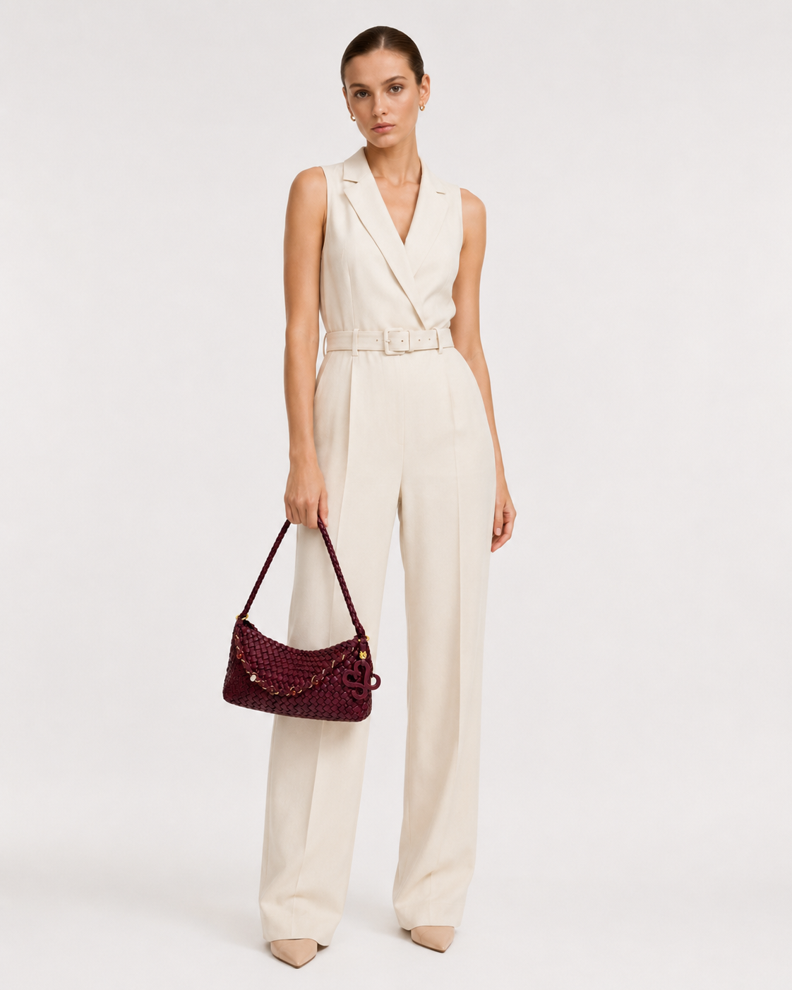 Full length view of a model in a cream jumpsuit carrying the THReAD burgundy woven shoulder bag