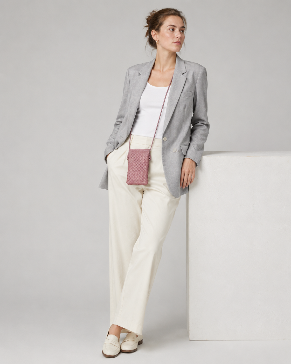 Elegant model in a grey blazer wearing the dusty rose woven phone bag across the body
