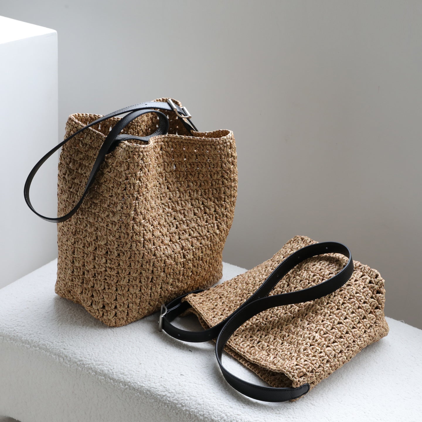 Two natural raffia hobo bags displayed together showing the genuine leather straps