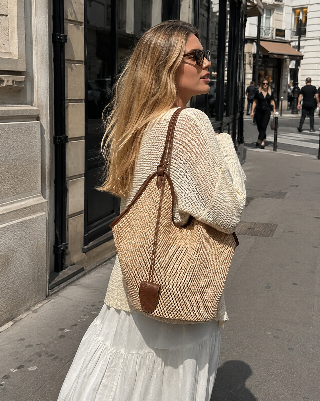Woman walking in the city with a woven shoulder bag in a relaxed street style scene