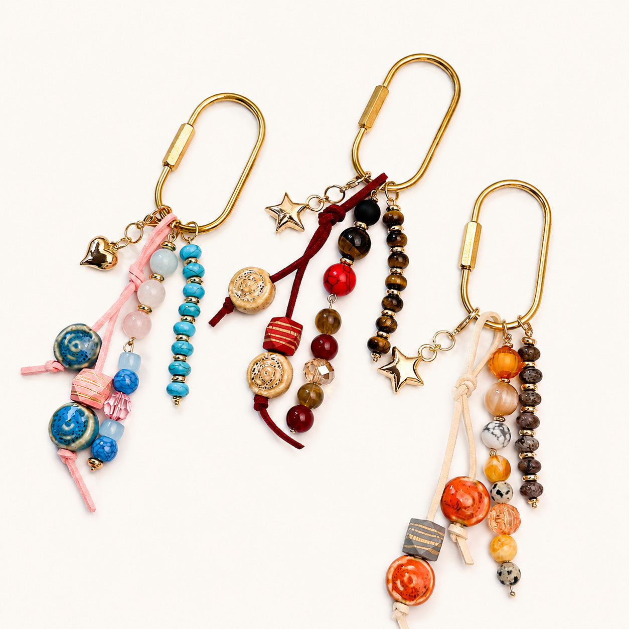 Three beaded pin bag charms in pink-blue, burgundy-tigereye, and orange-earth tone colorways