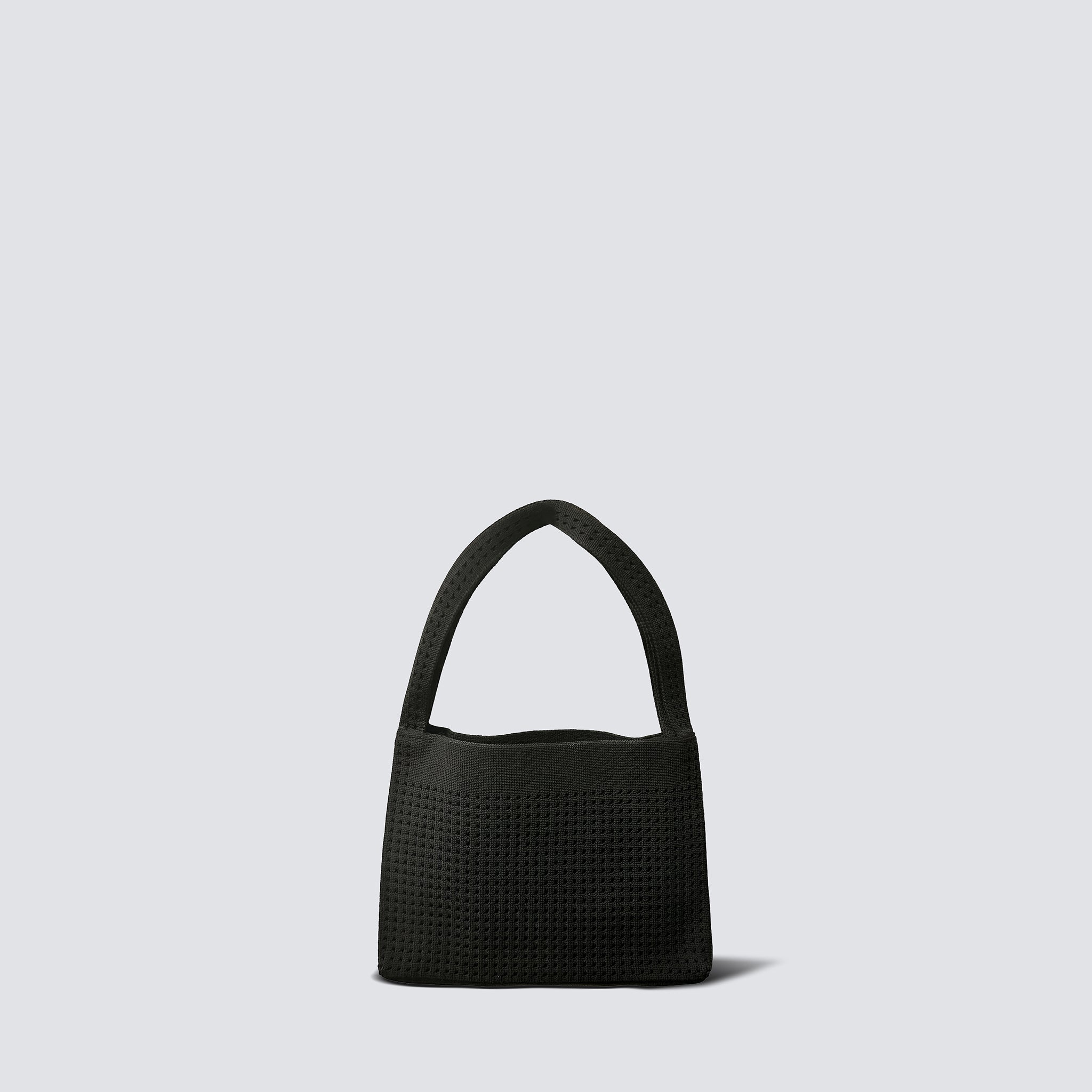 Minimalist black knit mini bag with a curved top handle on a simple product background