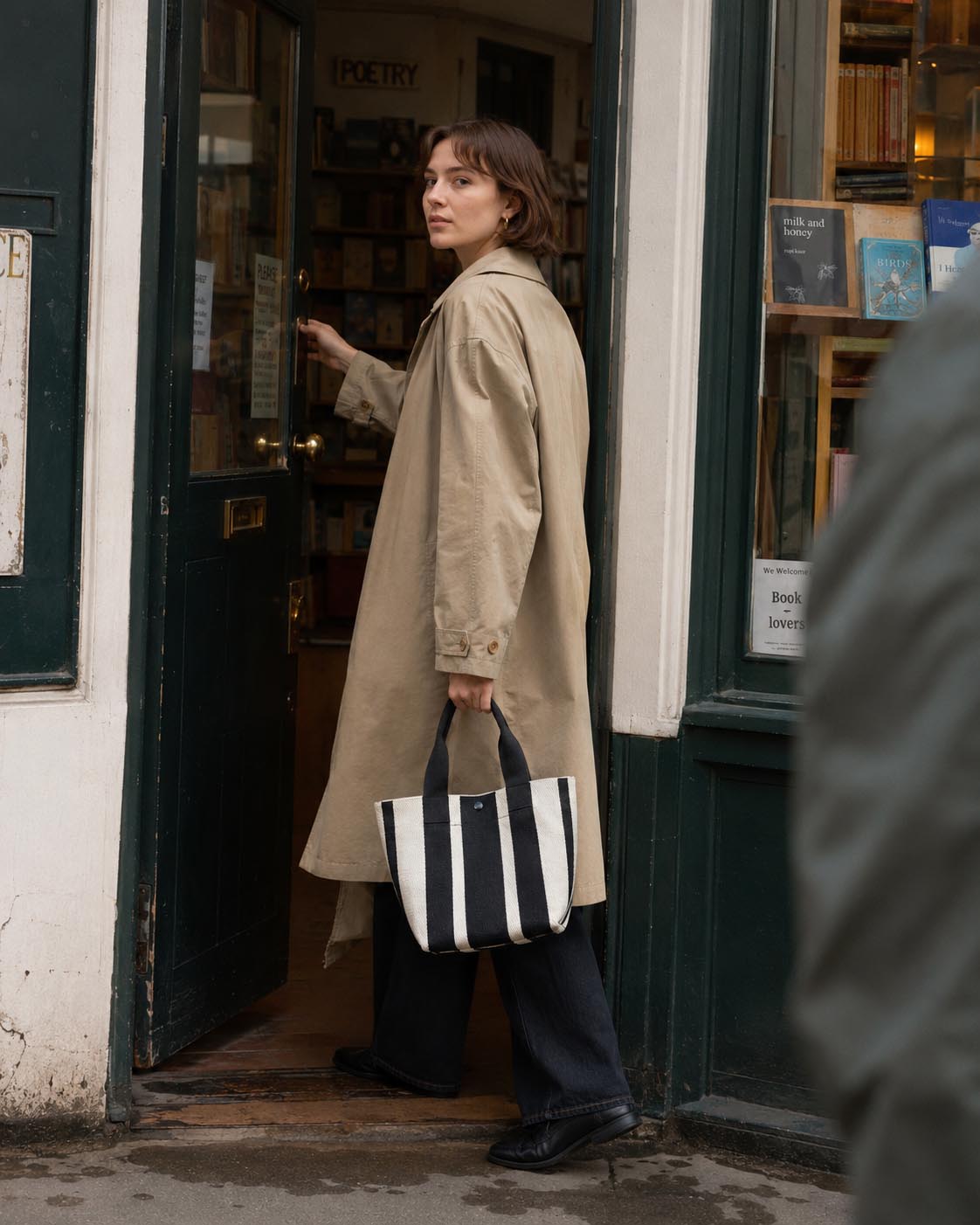 Woman carrying a black and white striped knit tote bag outside a bookstore