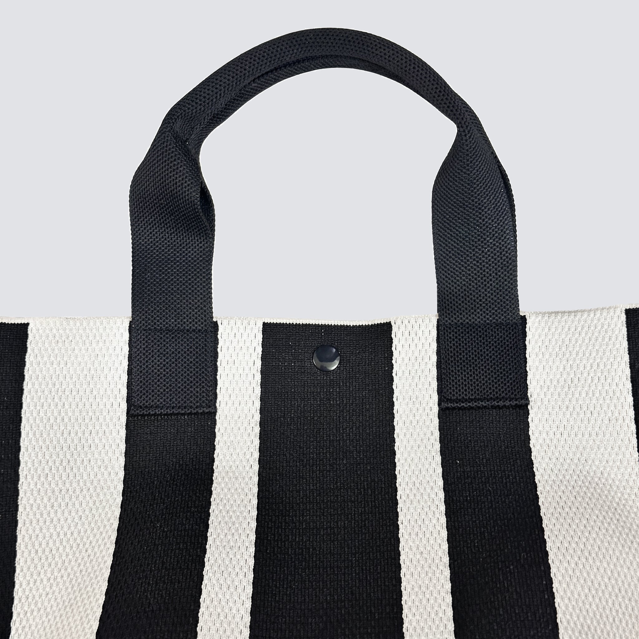 Side view of a black and white striped knit tote bag with short handles