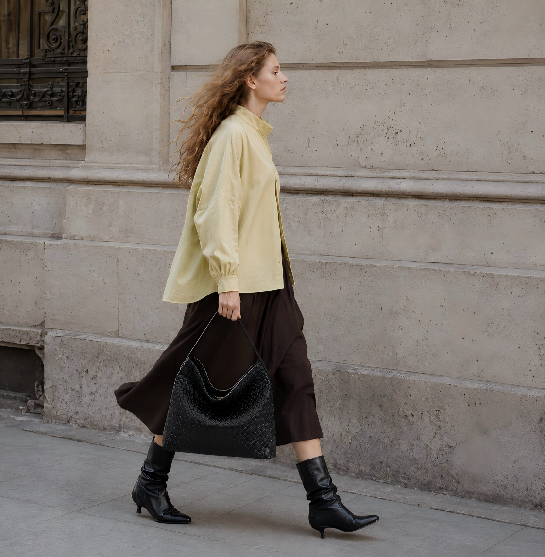Woman walking with a black woven slouchy tote bag in a relaxed street style scene