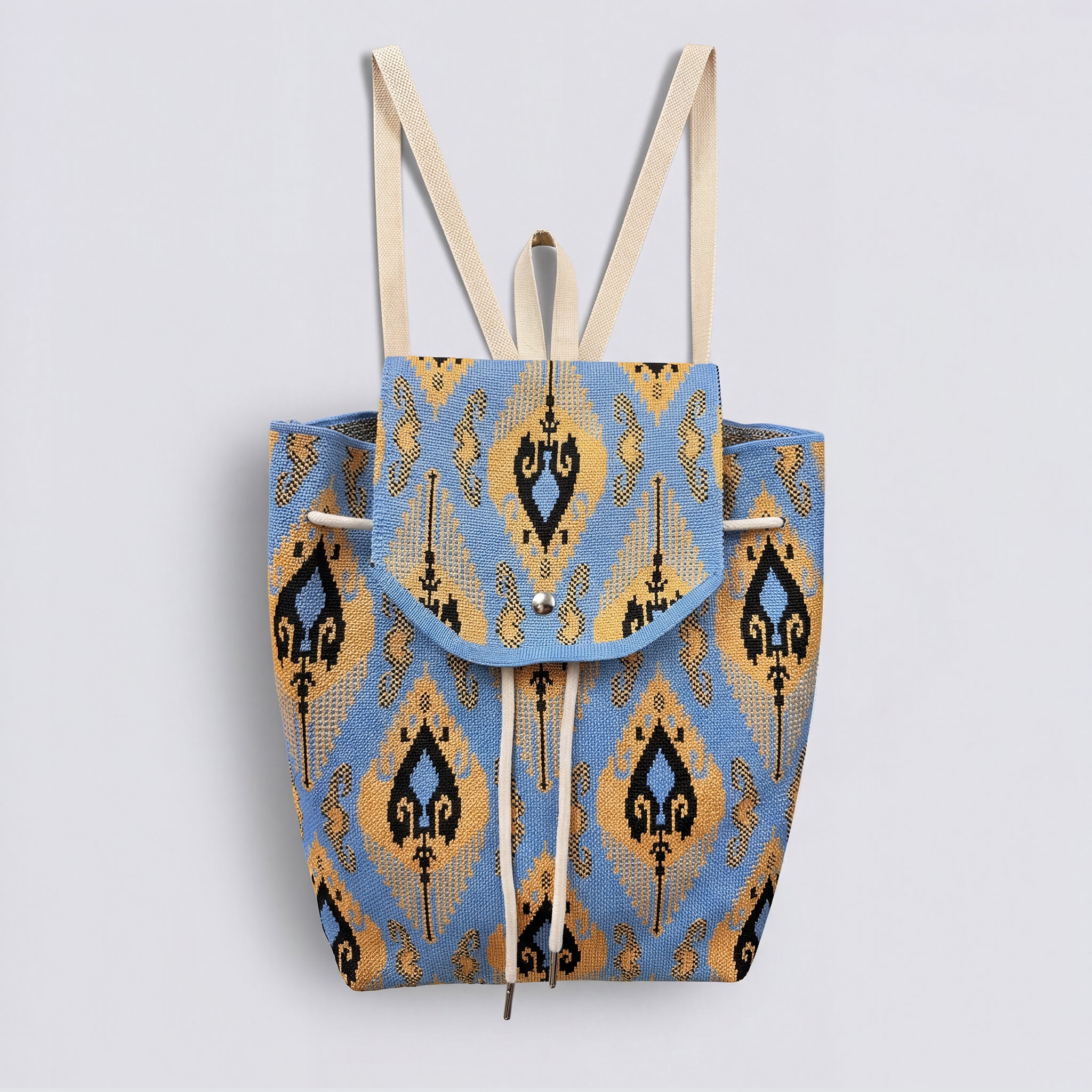 Blue and gold bohemian knit backpack with drawstring and flap closure on a simple product background