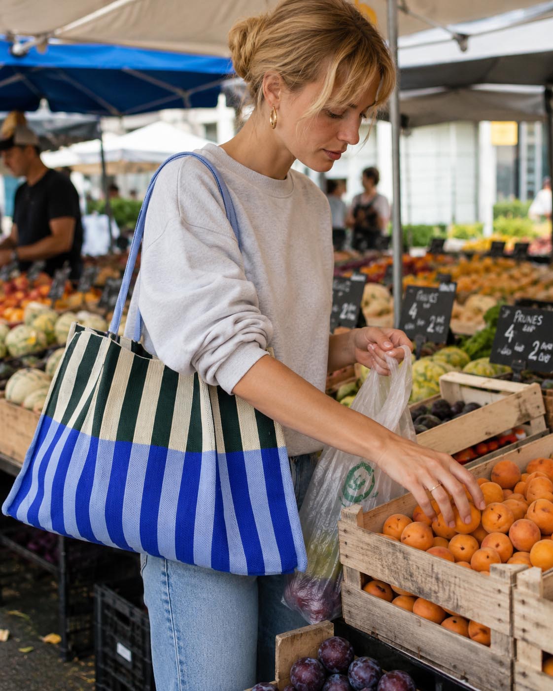 Woman carrying an oversized blue and green striped knit tote bag at a farmers market