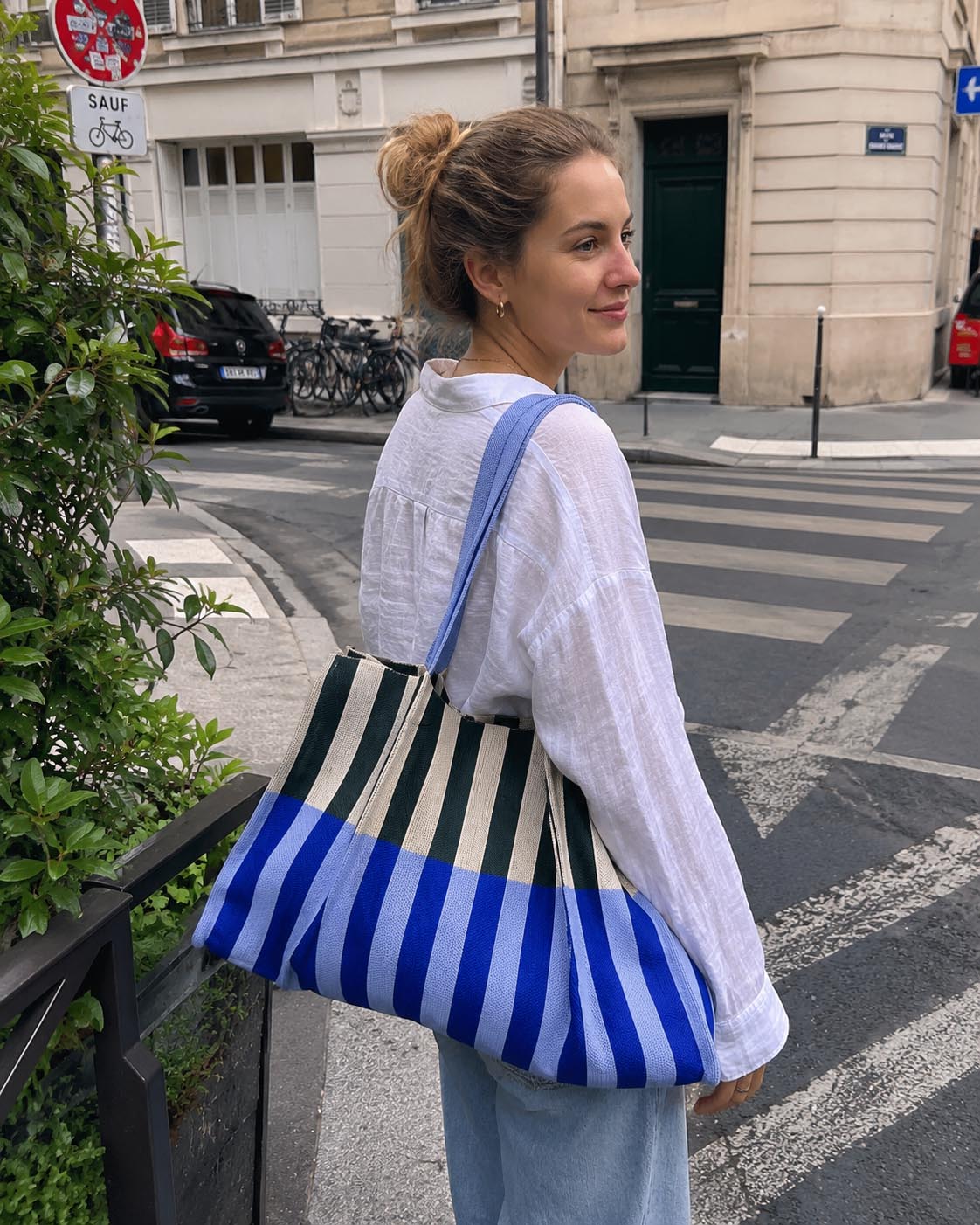 Woman on a Paris street with an oversized blue and green striped knit tote bag over her shoulder