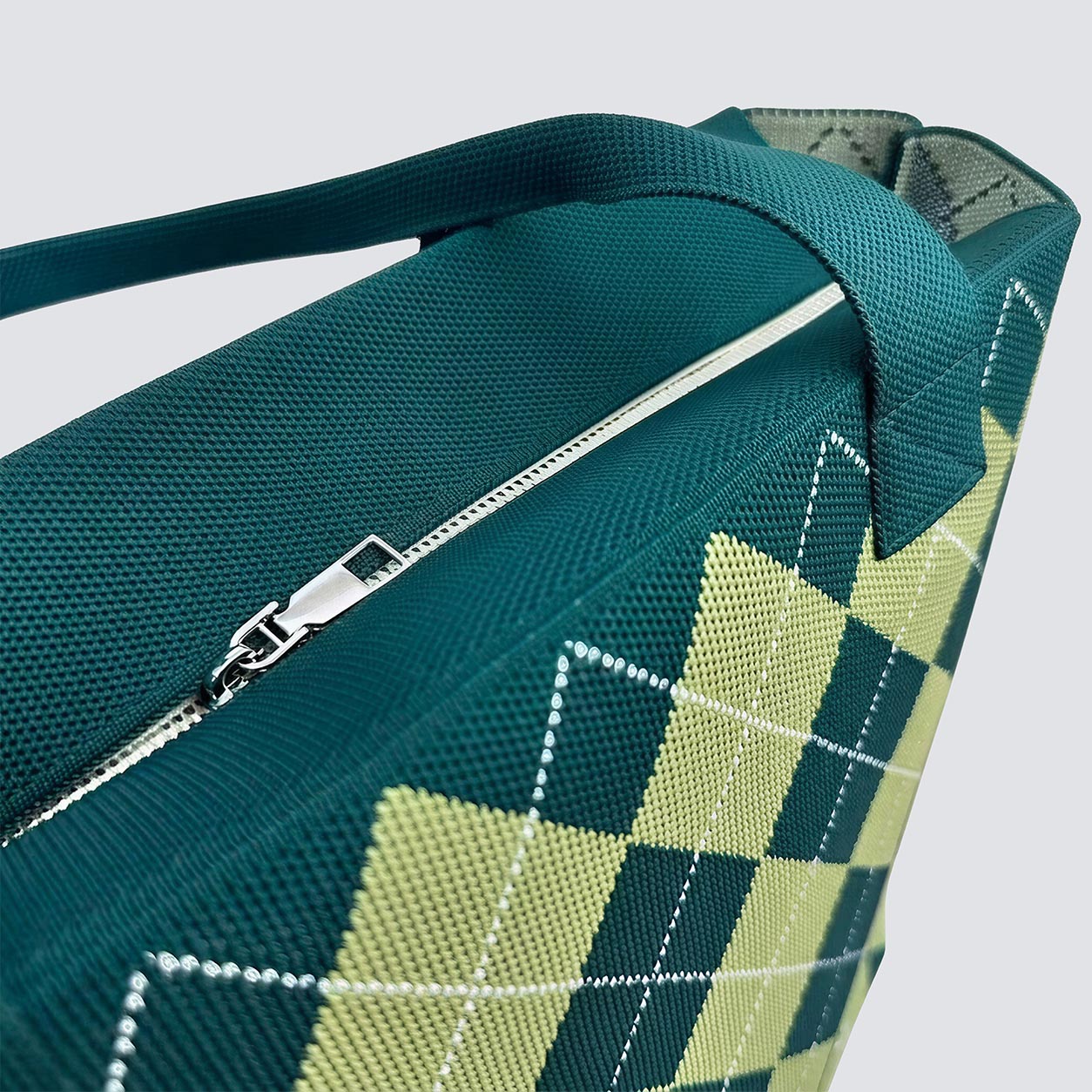 Close-up of green argyle knit tote bag zipper and handle detail
