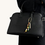 Green and white beaded bag charm with ceramic beads hanging from a black handbag