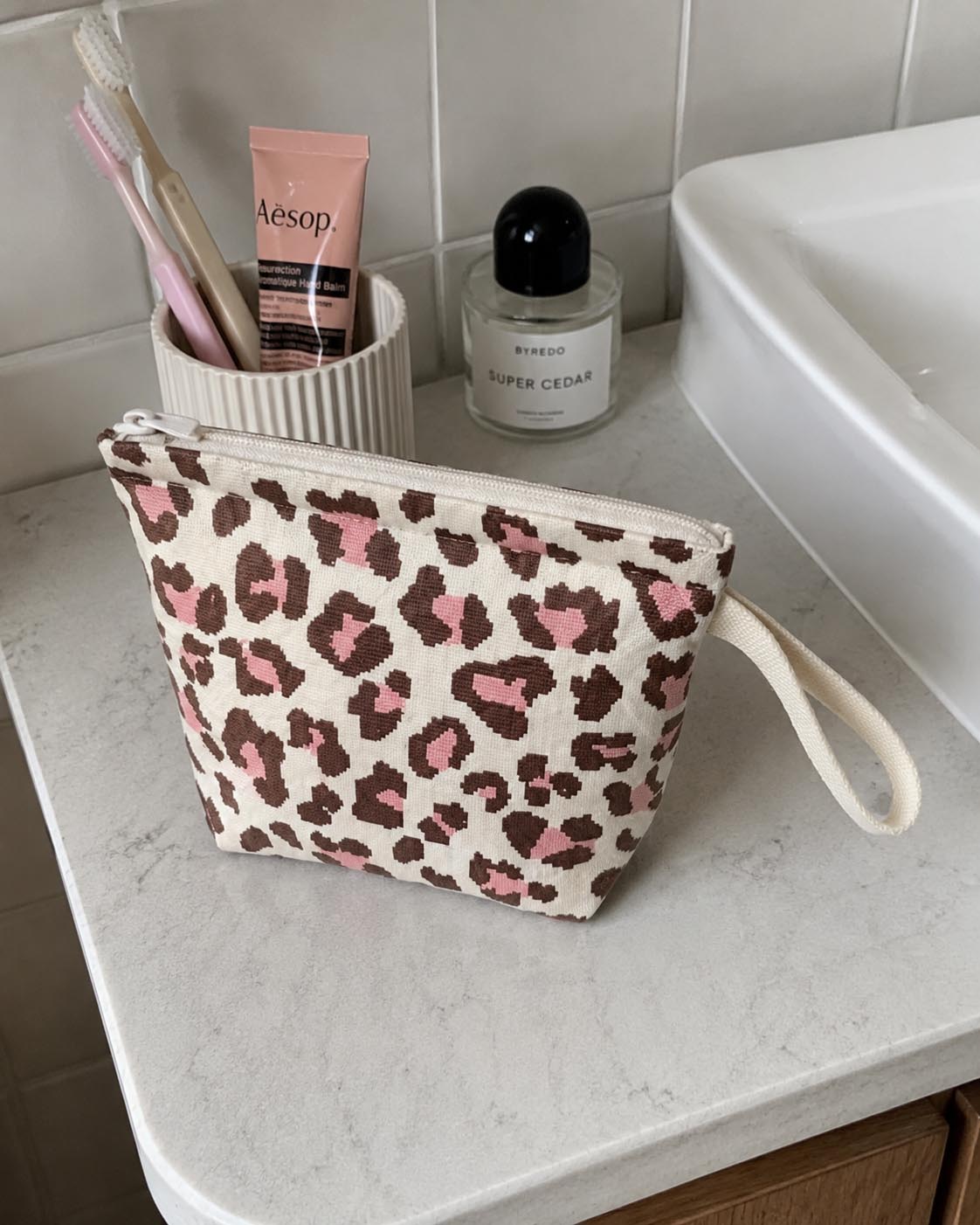 Leopard print mini pouch sitting on a bathroom countertop styled with skincare