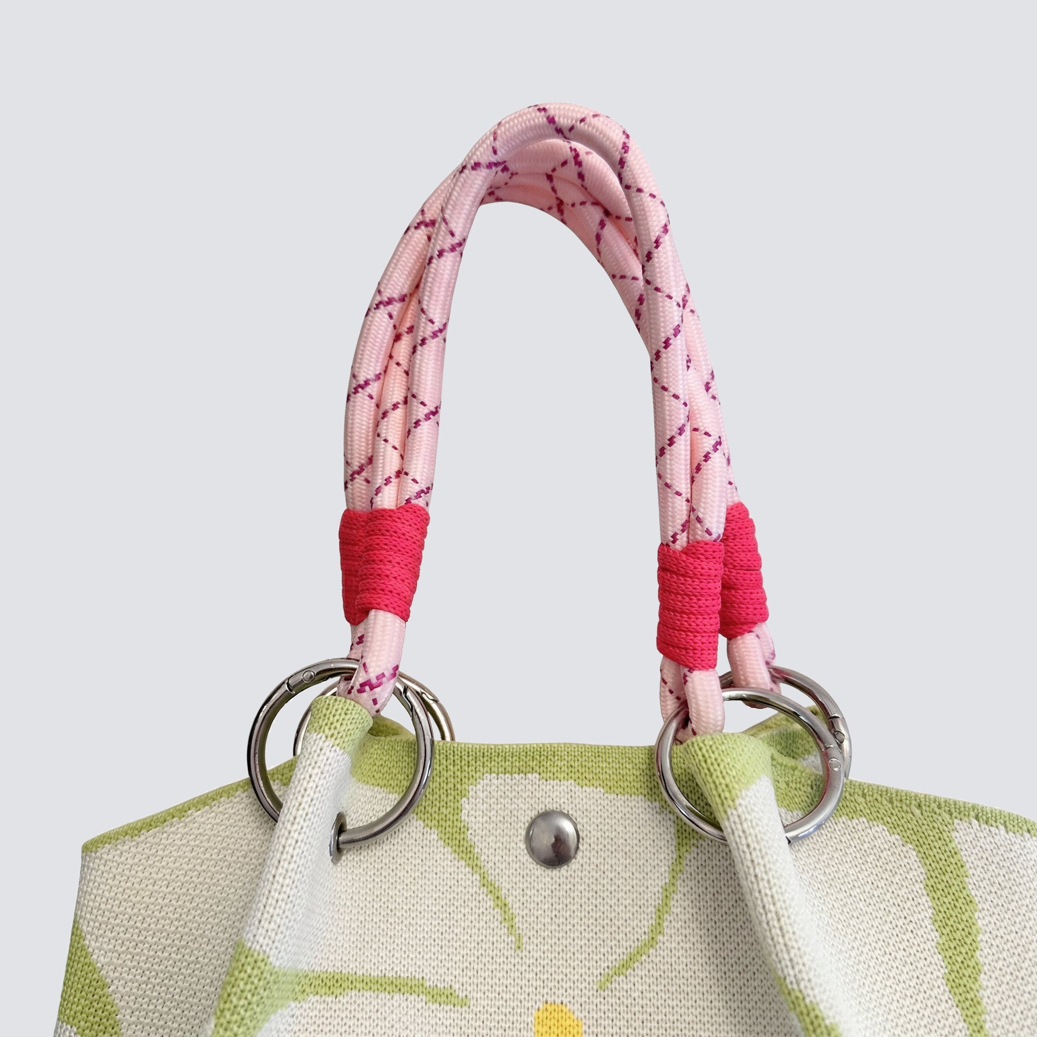 Drawstring and pink handle detail on a light green patterned knit mini tote bag