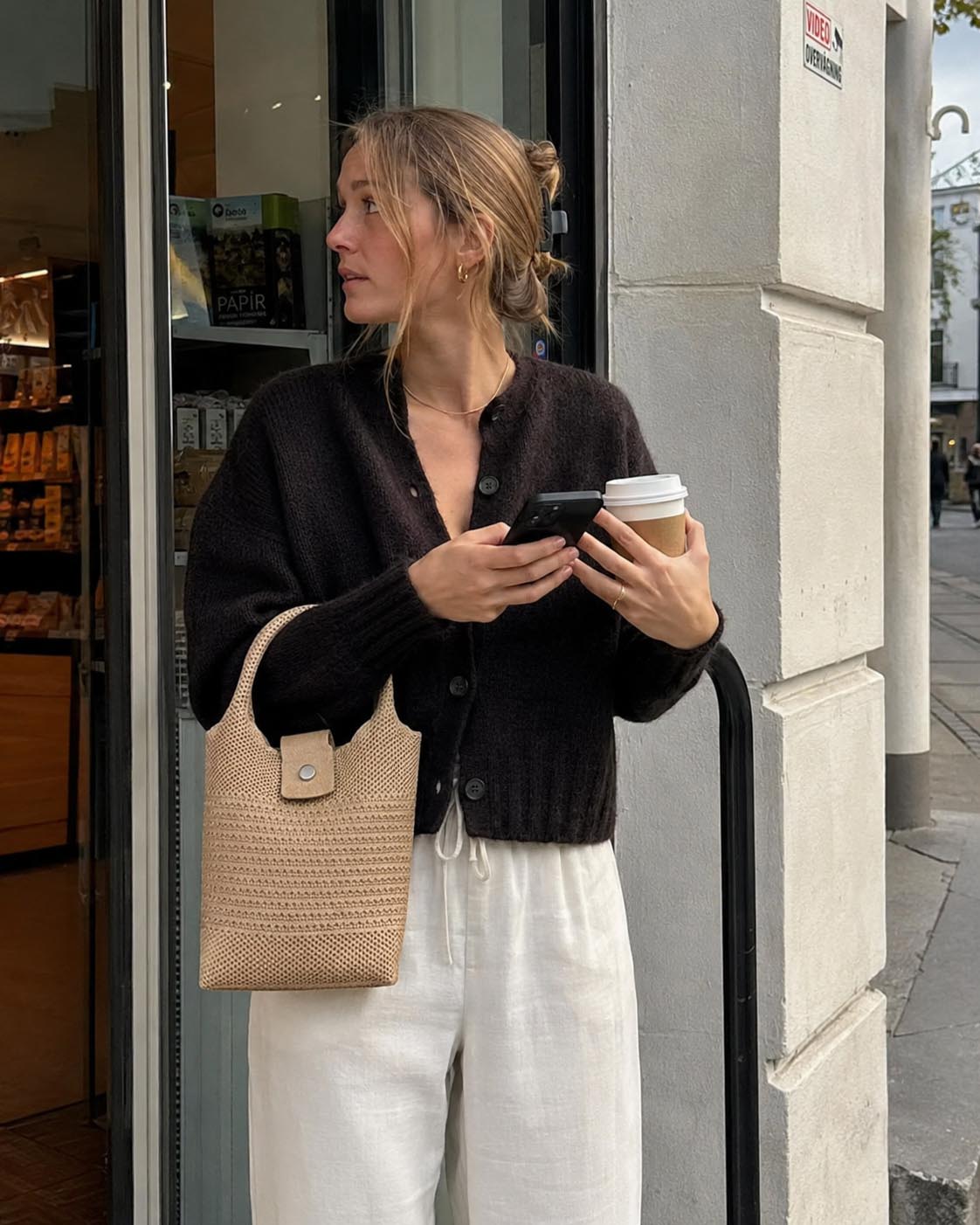 Woman carrying a natural woven mini tote bag while holding a coffee on a city street