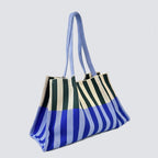 Side view of an oversized blue and green striped knit tote bag with long straps