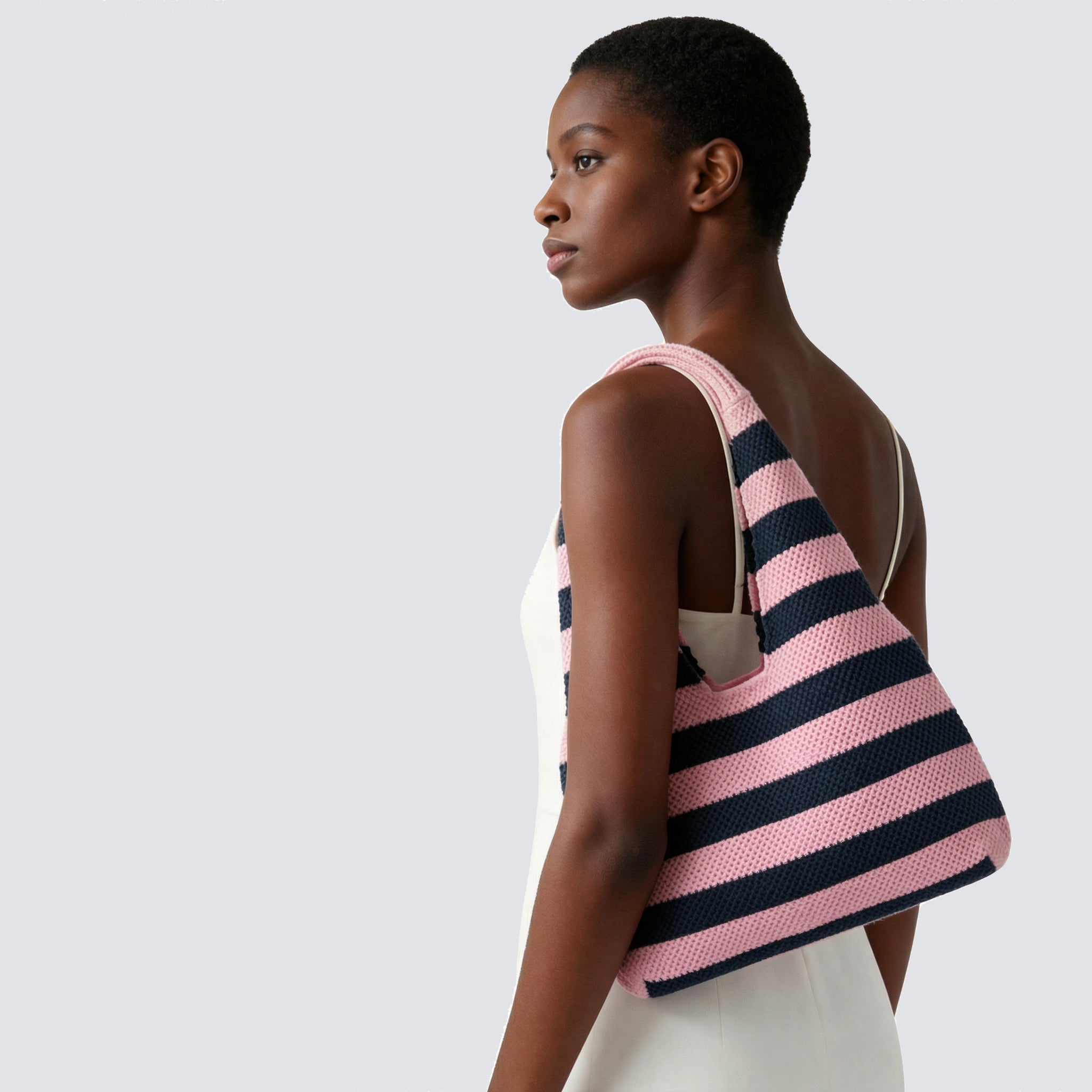 Woman carrying a pink and navy blue striped knit beach bag with a summer outfit
