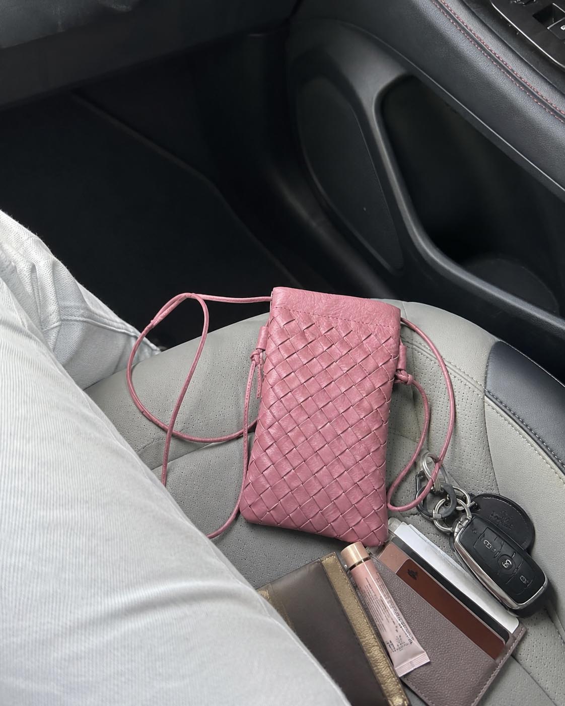 Pink woven vegan leather phone pouch styled in a car lifestyle scene