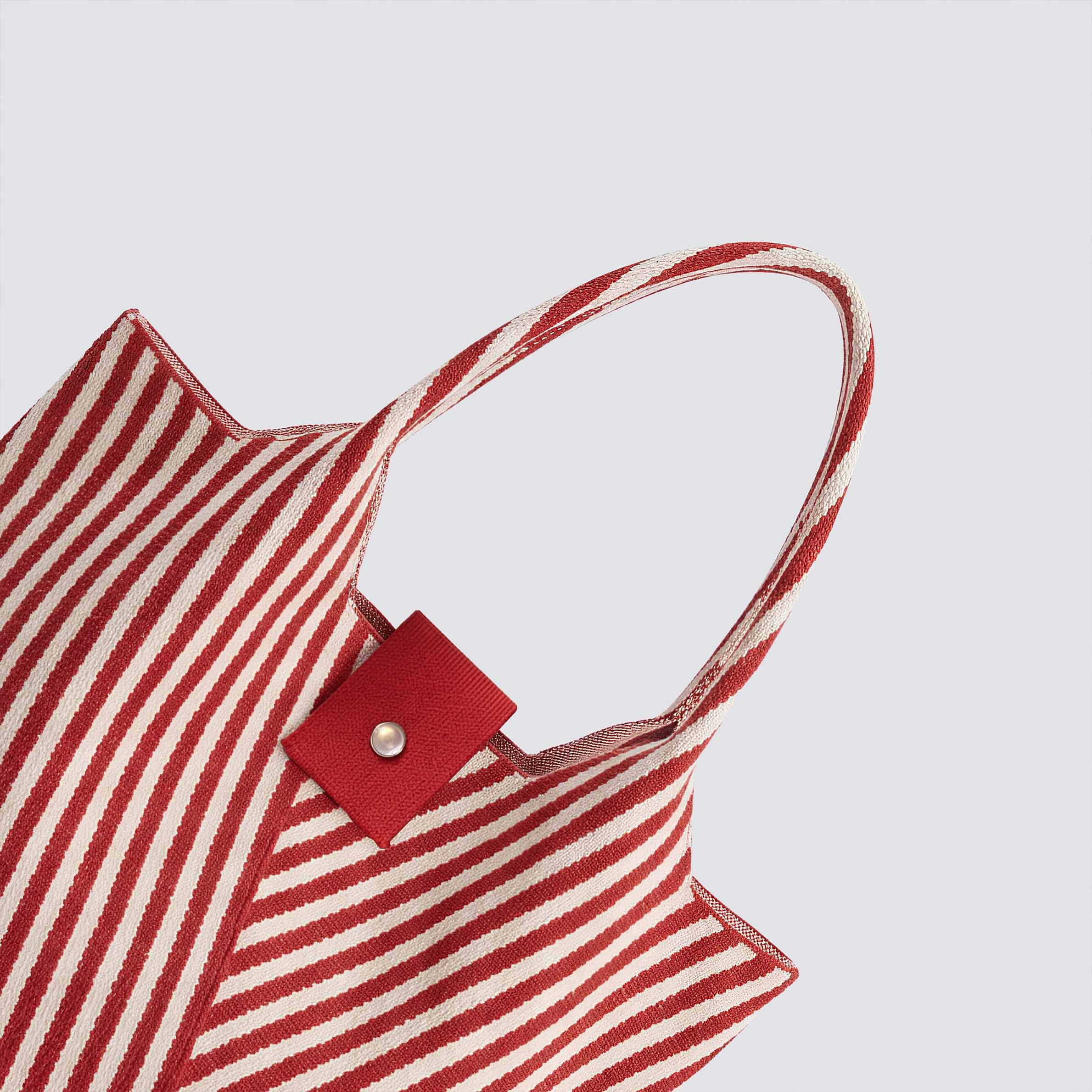 Close-up of the snap closure and woven strap detail on a red and white striped knit tote bag