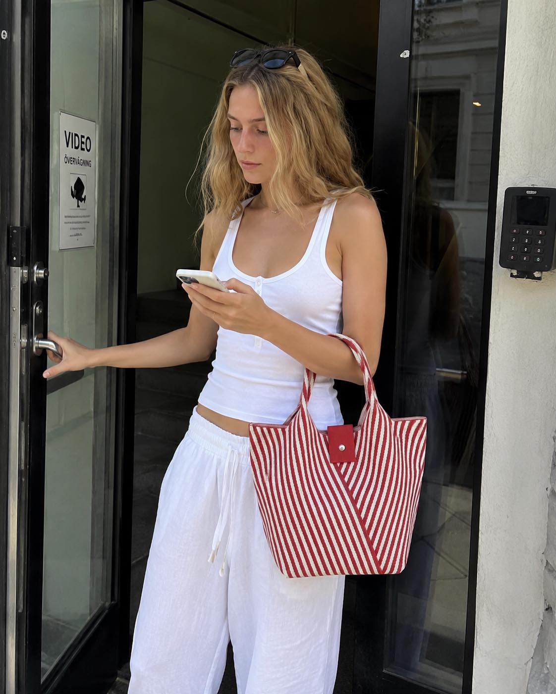 Woman on the street carrying a red and white striped knit summer tote bag with a casual white outfit