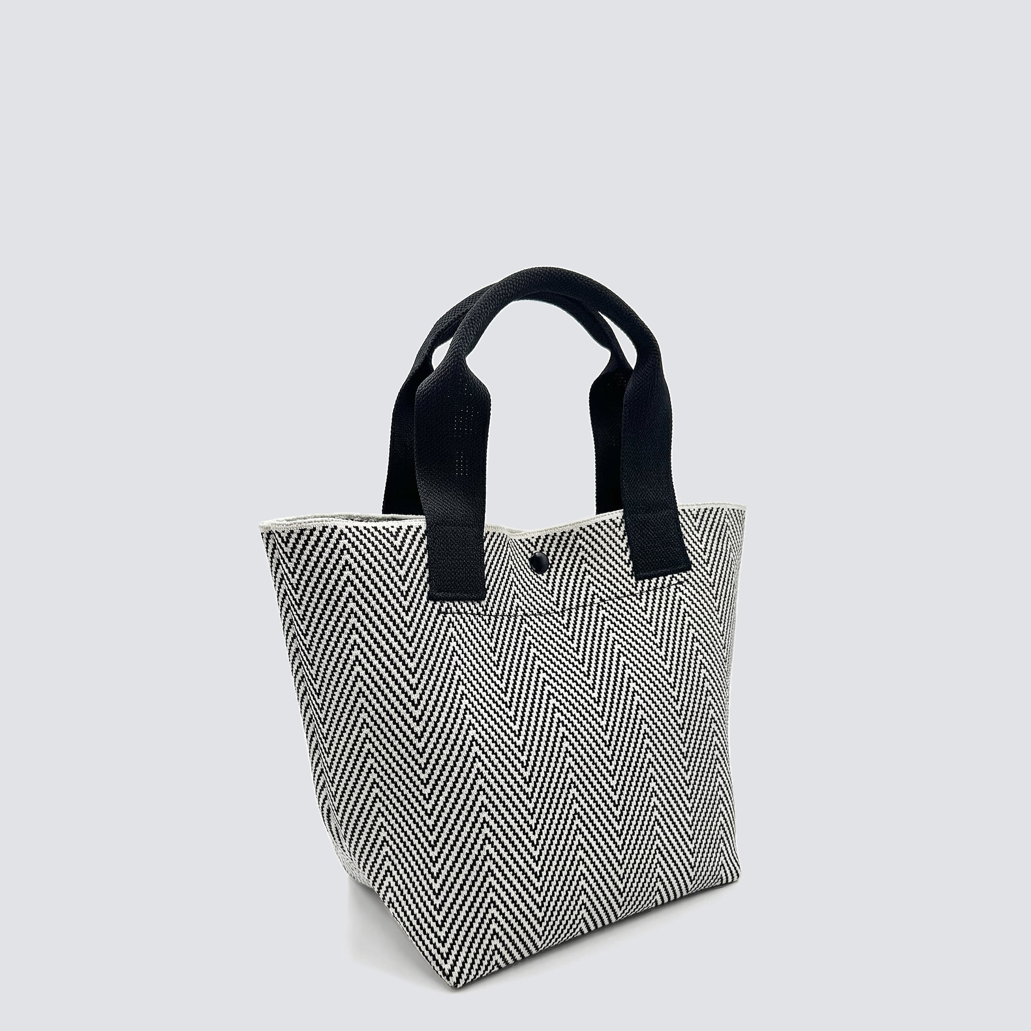 Side view of a textured black and white knit tote bag with black handles