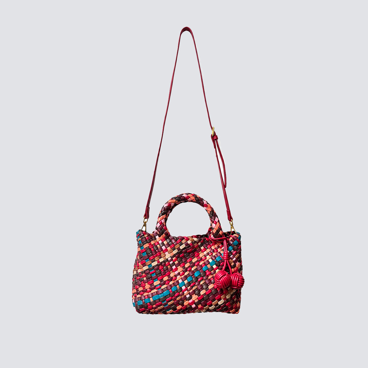Multicolored woven crossbody commuter bag hanging by its long adjustable red vegan leather strap