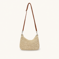 Front view of a natural woven paper straw crossbody beach bag with a long brown strap