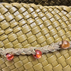 Macro detail of the green woven vegan leather pattern and the decorative braided strap with amber beads